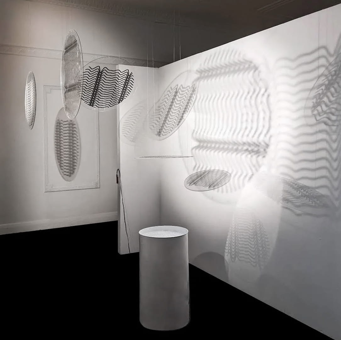 A photo of an installation with shadows of moiré pattern on the walls and a small pool with water