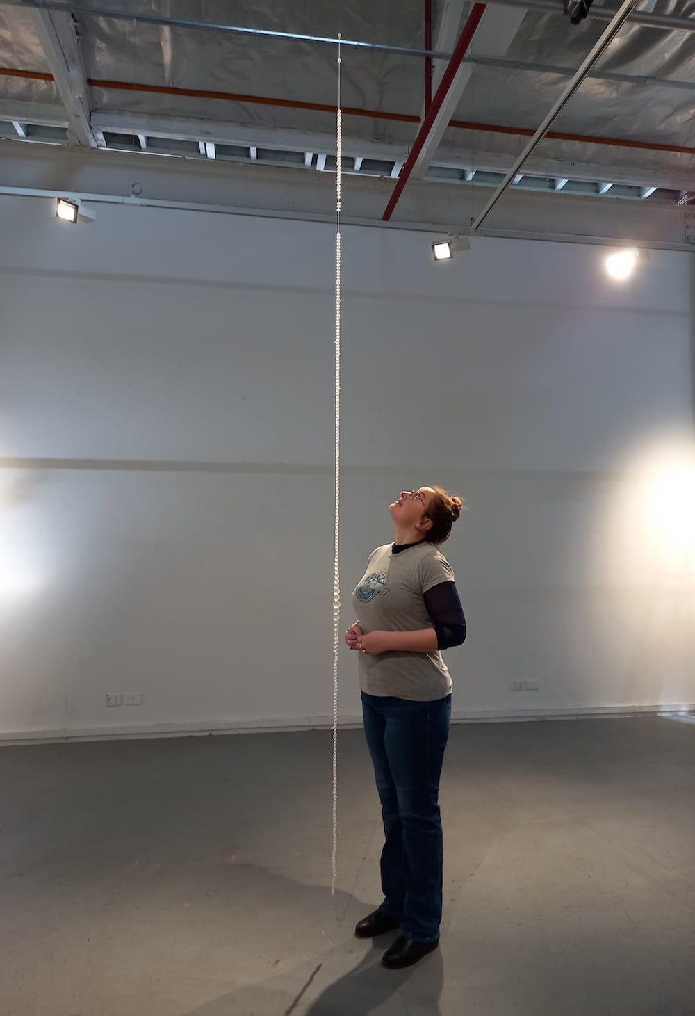 Long length of beads in bare room with the Artist standing next to it