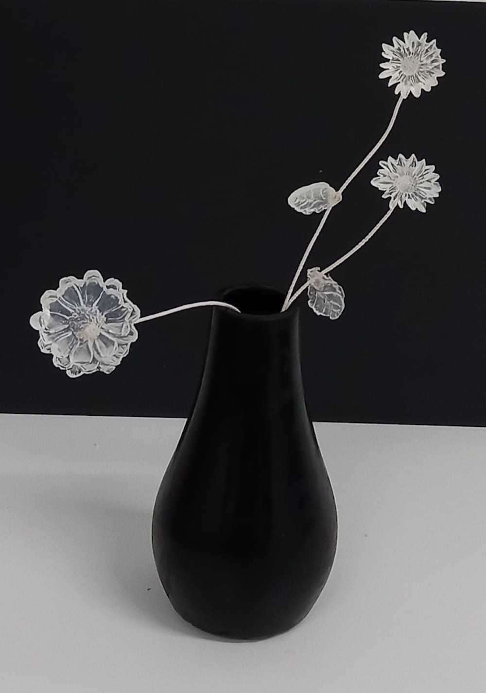 black vase with three flowers, on a white table with a black background