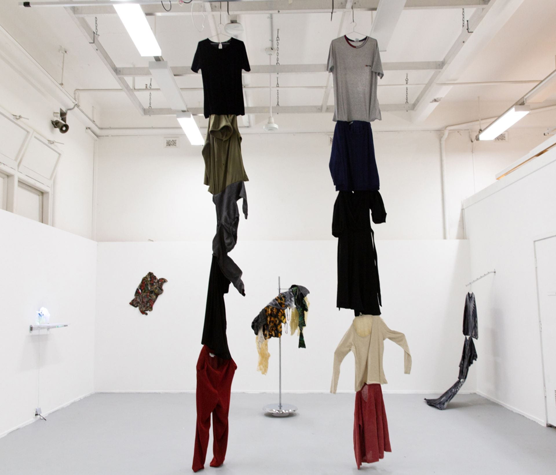 a line of clothing is hung from the ceiling, resin clothing artworks can be seen in background