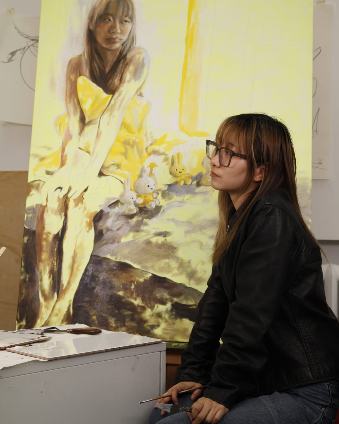 Photograph of the artist sitting next to her painting.