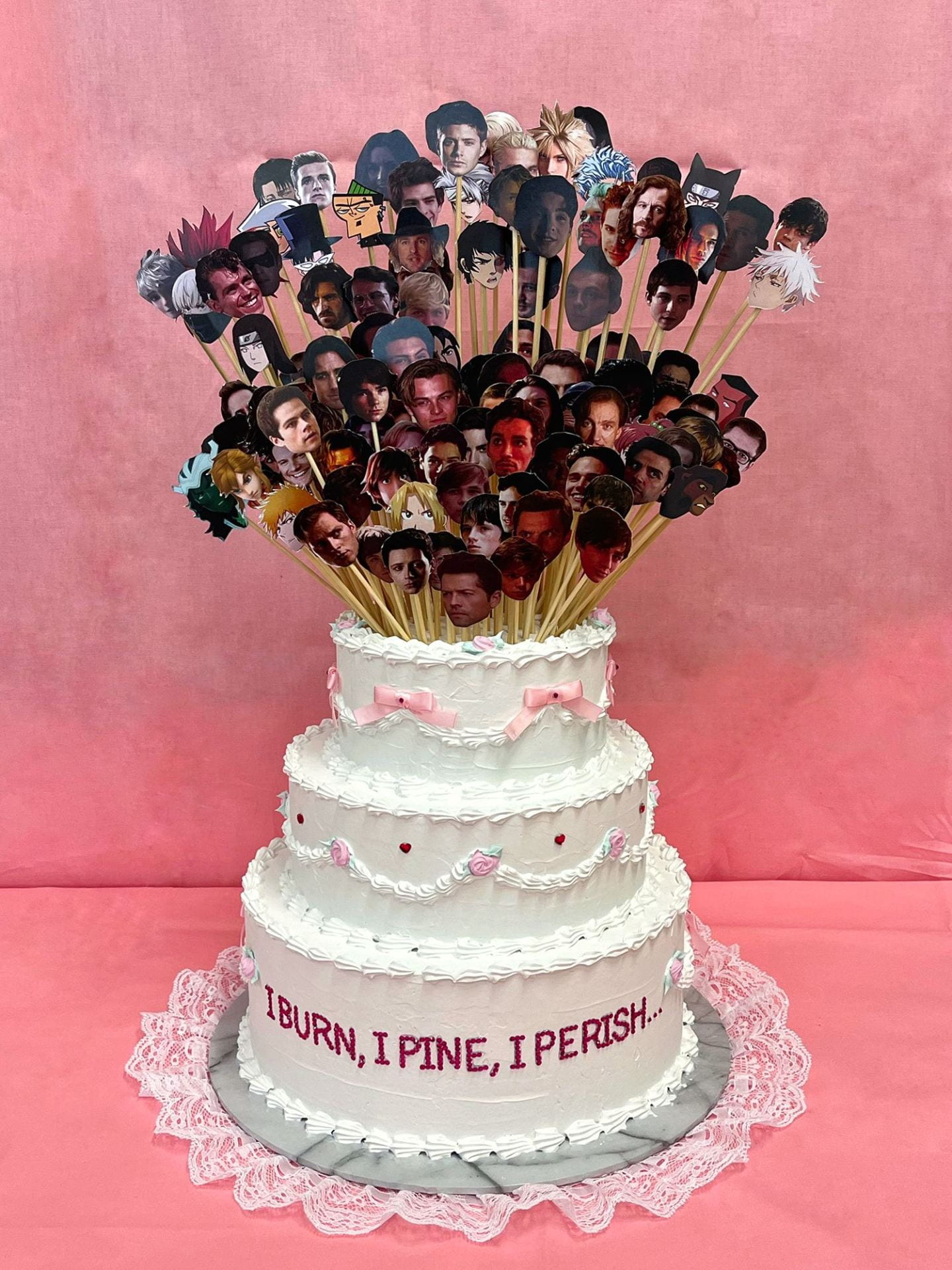 3 tiered wedding cake, featuring a series of cake toppers along with rhinestone text reading 'i burn, i pine, i perish...'