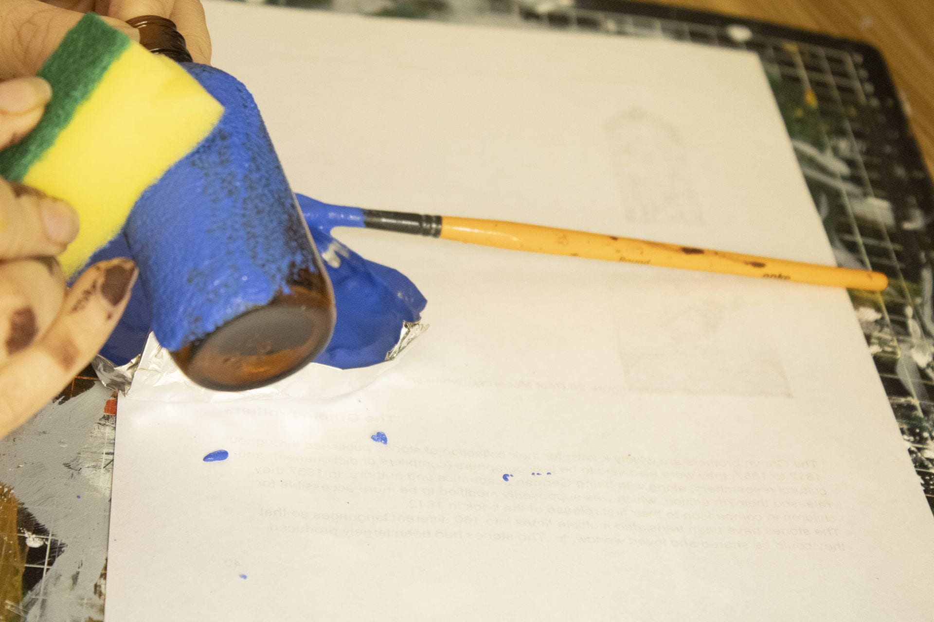 Using a sponge to apply blue paint to a glass bottle