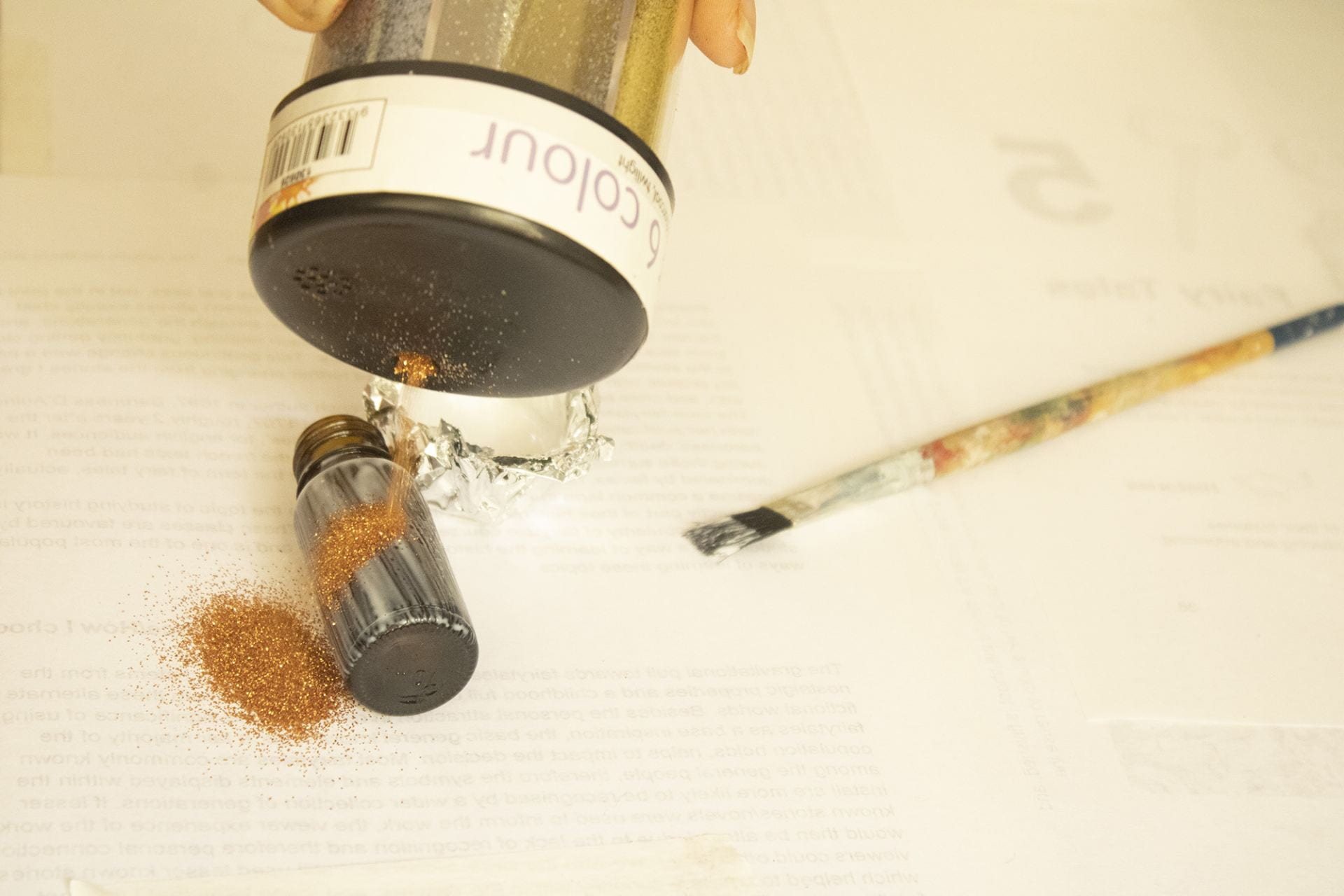 Rose gold glitter pouring onto a bottle with a paint brush to the side