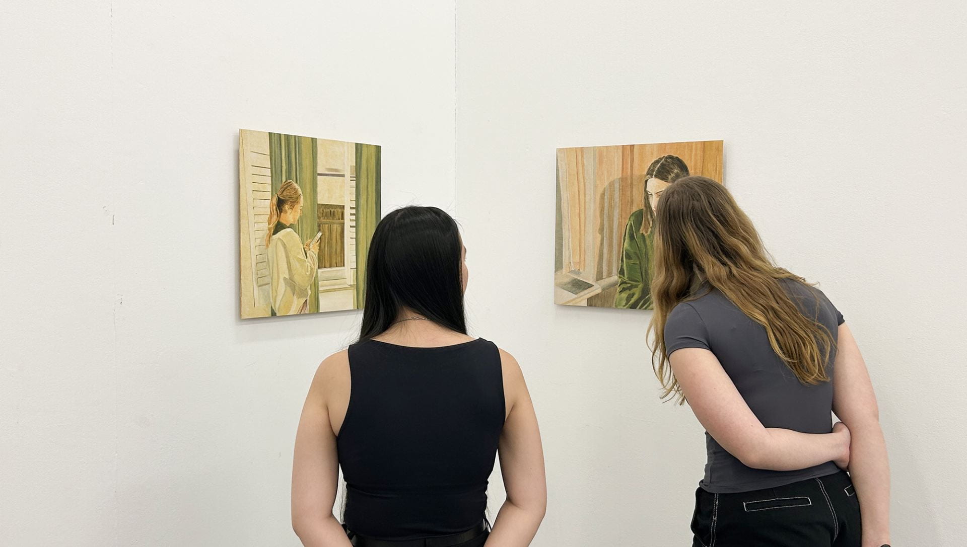 two viewers looking at two figurative paintings hung in a corner