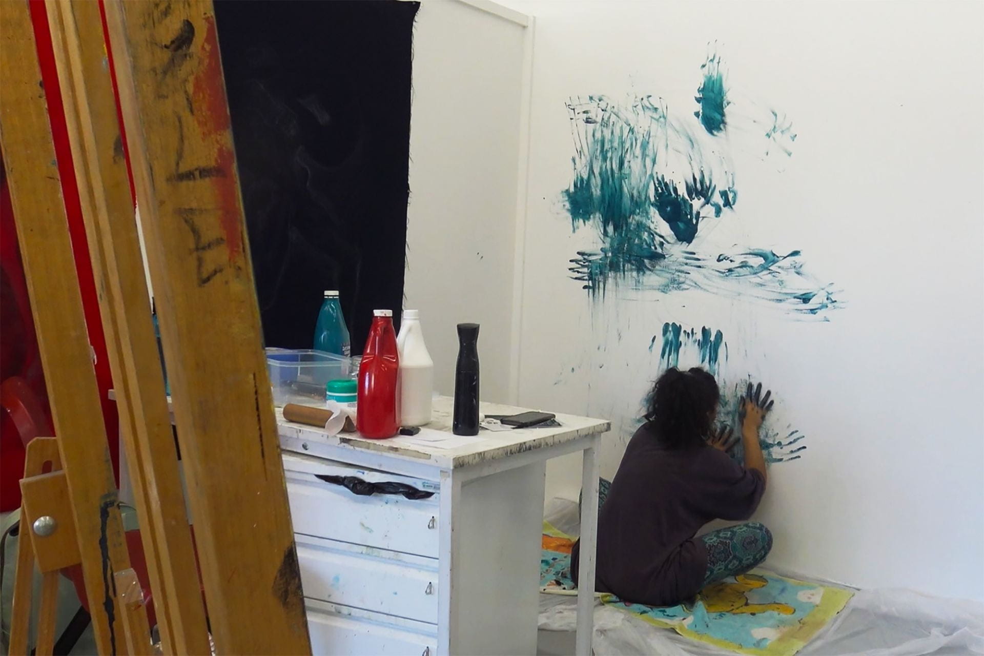 artist sitting on the floor hand painting on the wall with blue acrylic paint