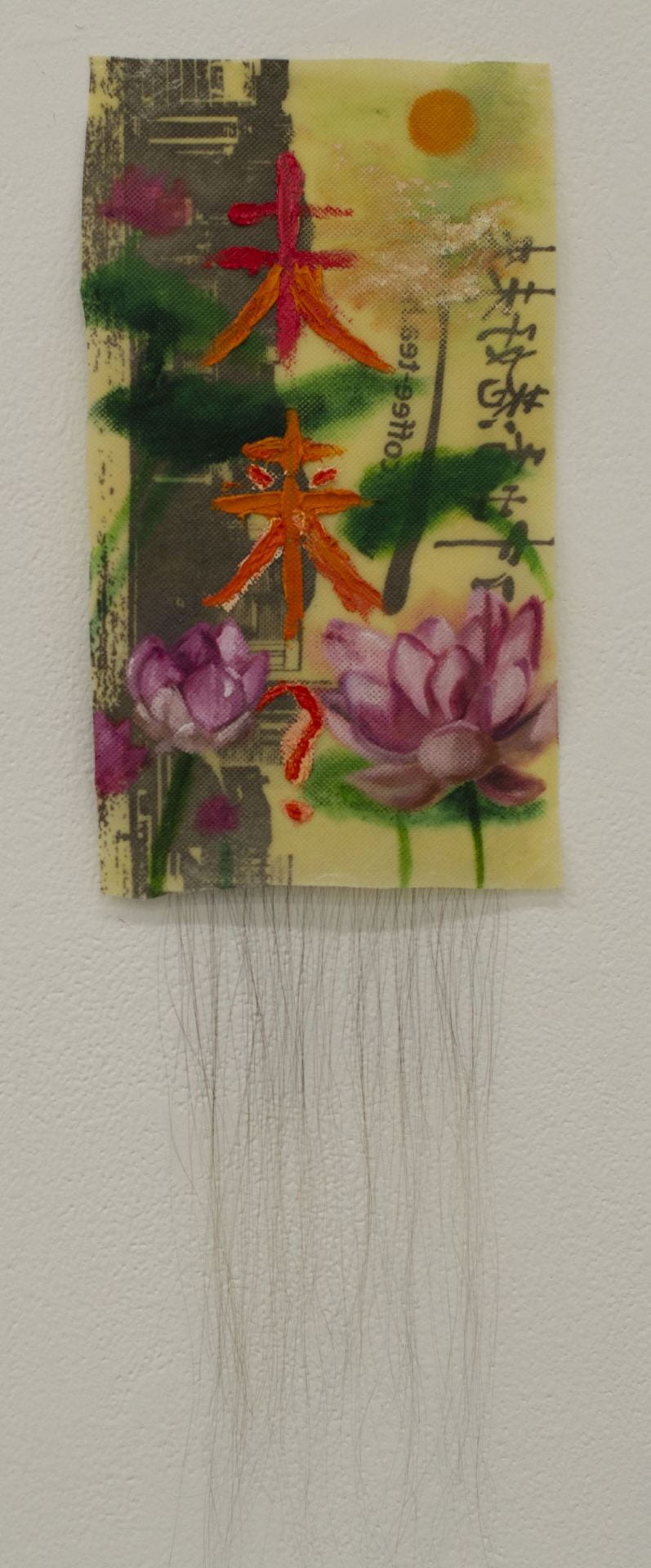 Painting. A rectangular fabric with lotus flowers, a sun, and the chinese words for 'future?' on it. Hair is attached to the bottom of the painting.