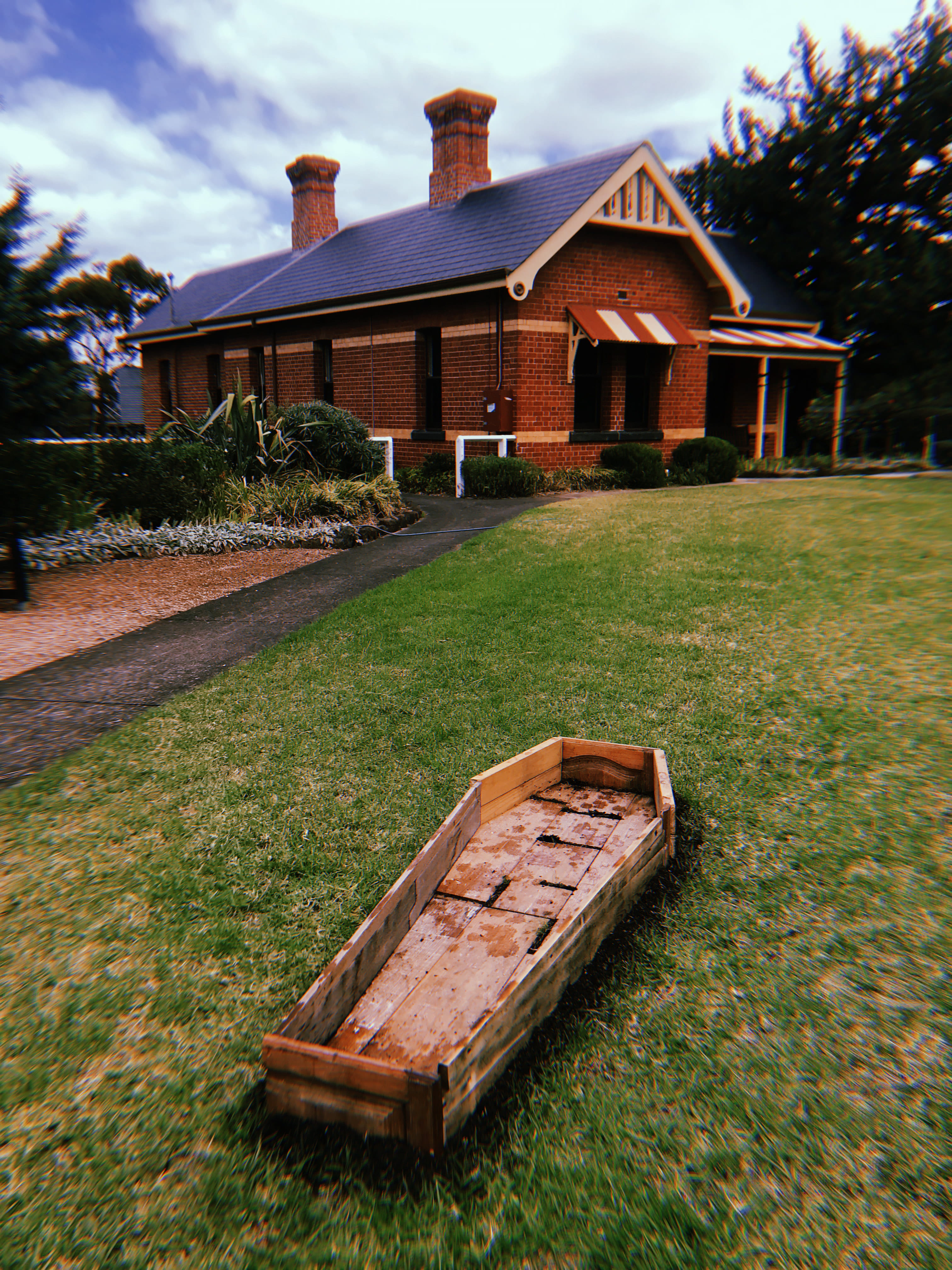 Photography of a coffin made from old wooden furniture lied on the grass.