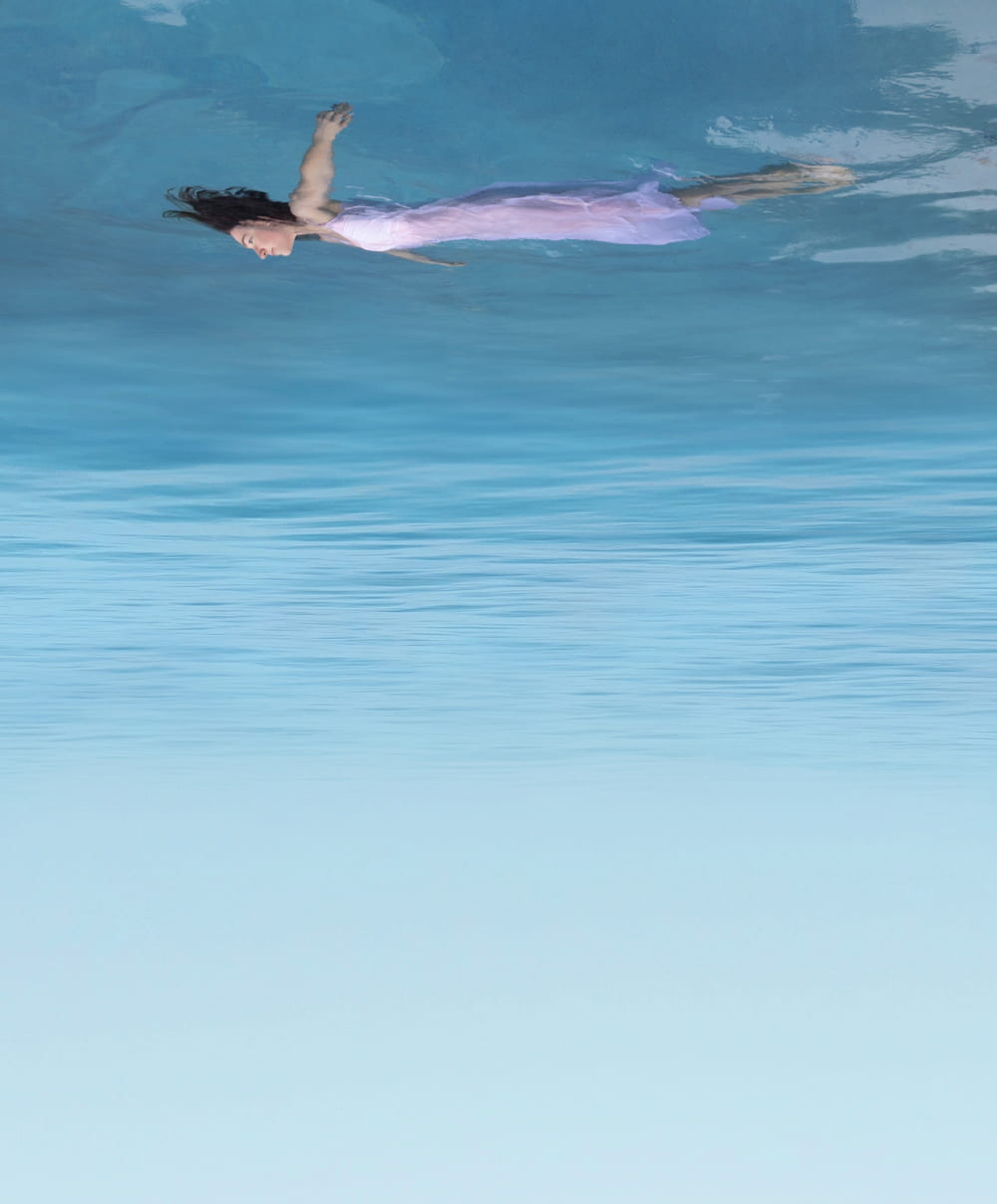 Photograph of a girl floating in the water in the perspective of the sky