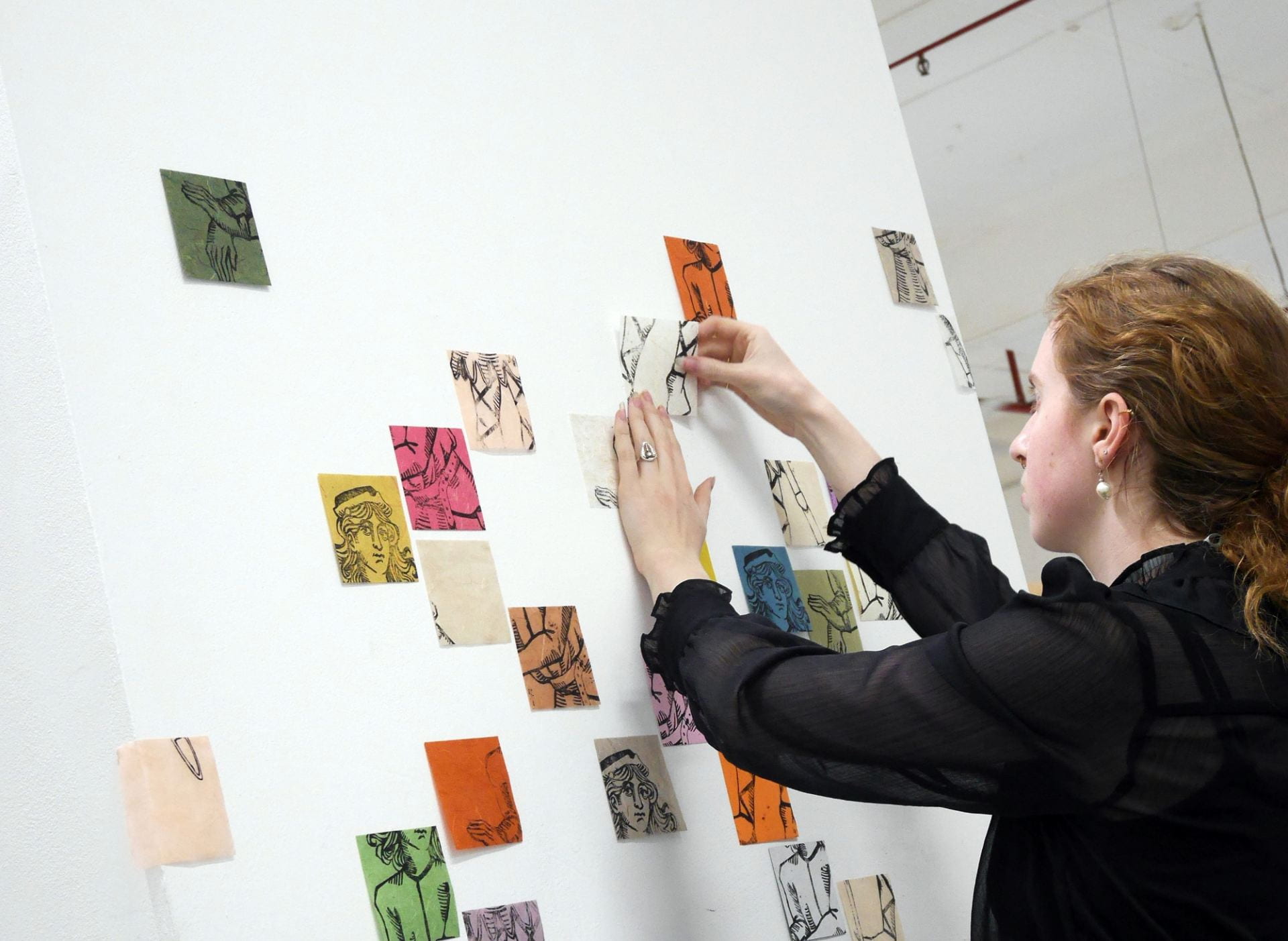 Artist installing various small woodcut prints on a white wall, not unlike a mosaic.