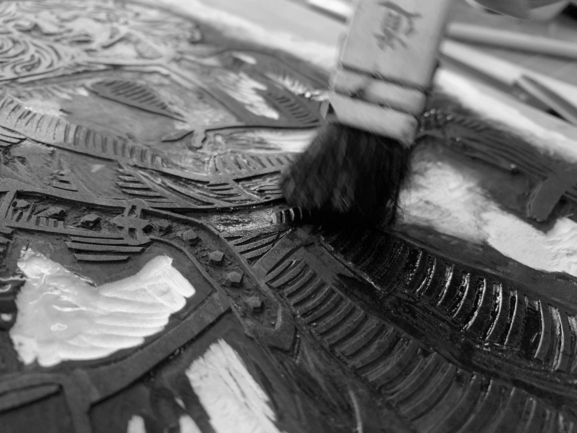 Close-up black and white image of a woodcut plate being inked up with a small brush.