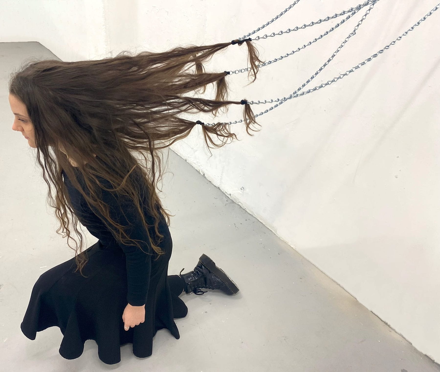 Photograph of a performance trial involving hair connected to chains attached to the wall.
