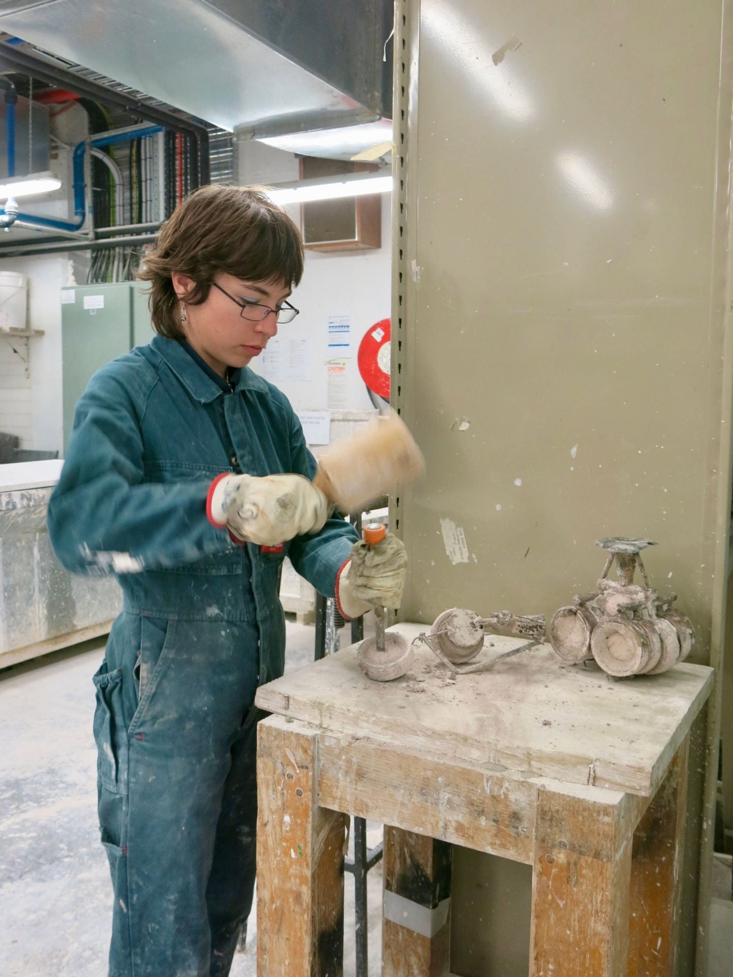 Photograph of a person removing investment from bronze using a chisel.