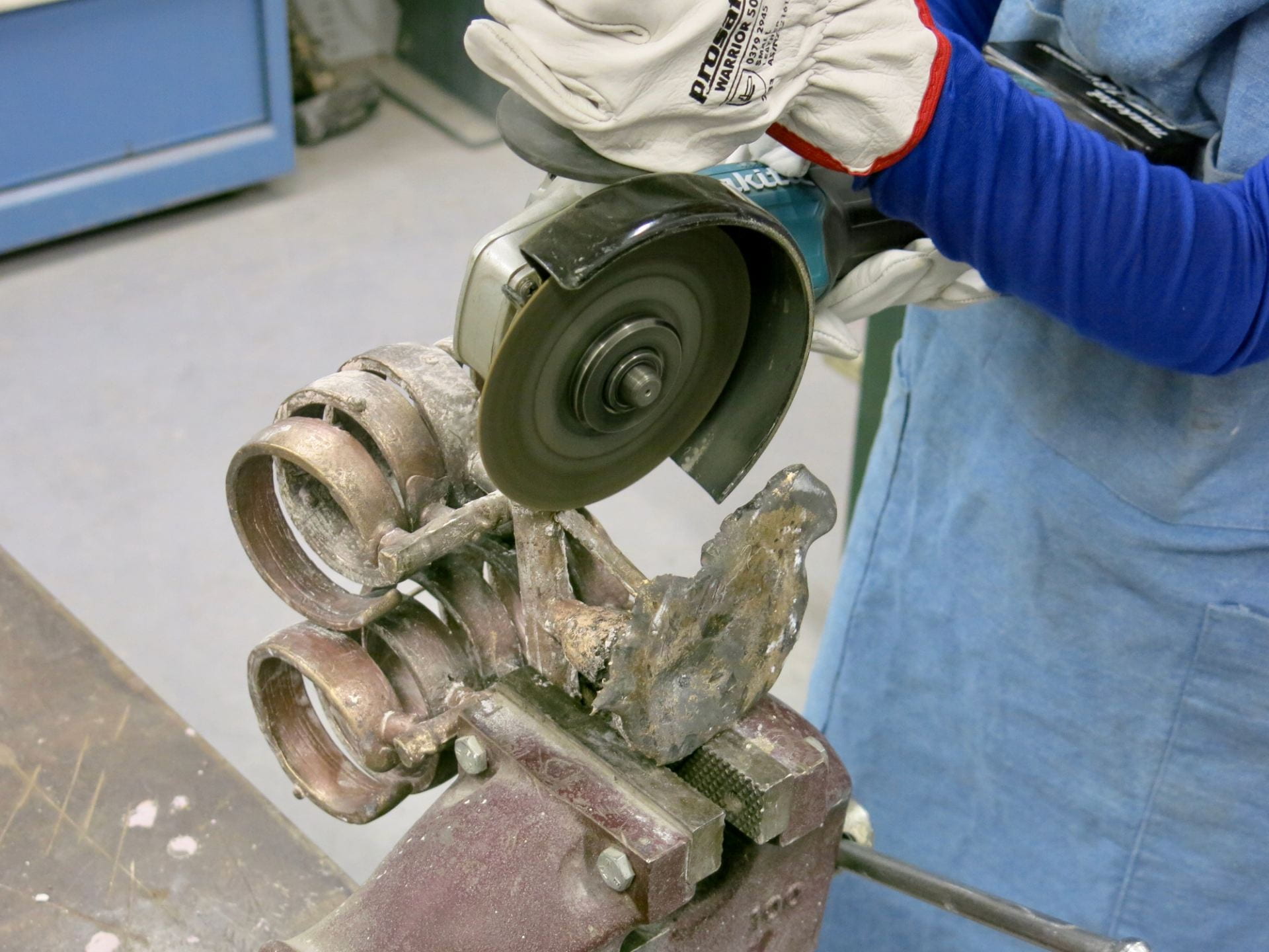 Person using an angle grinder to remove sprues from bronze objects.