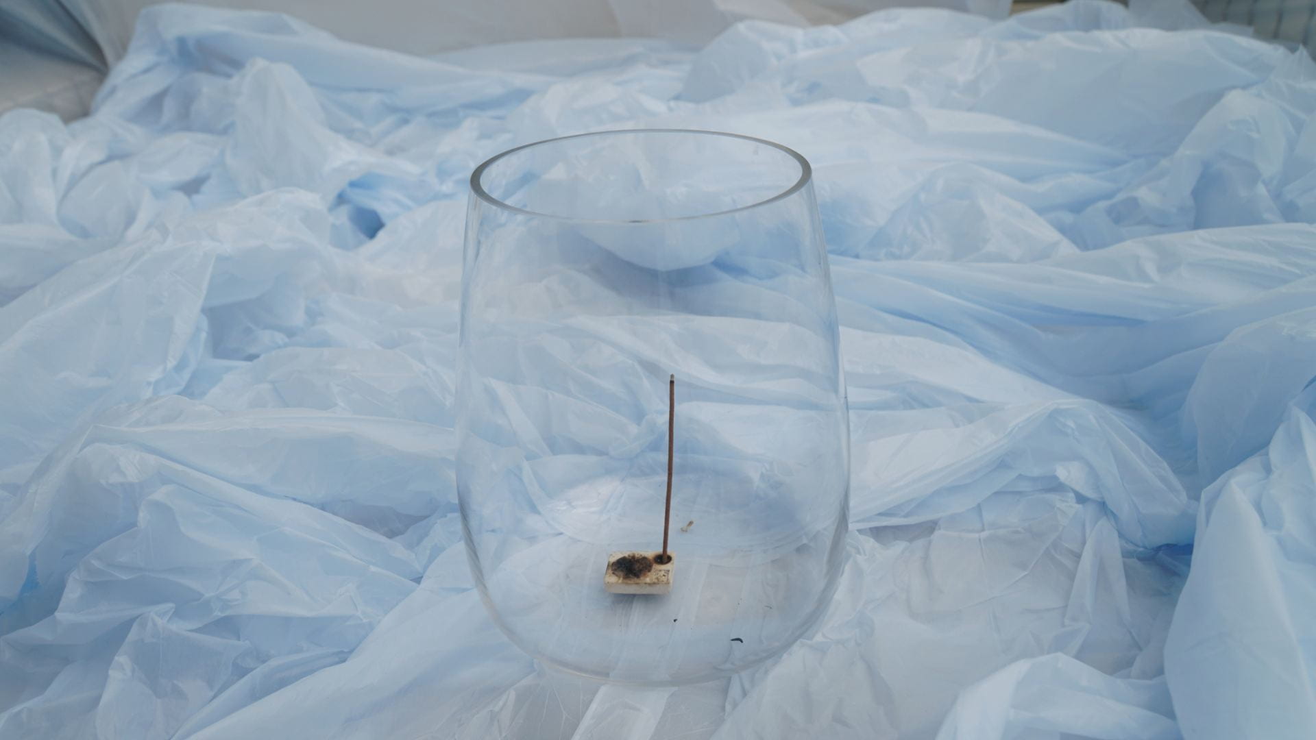 An incense burning in a glass jar surrounded by plastic tablecloths installed in the background.