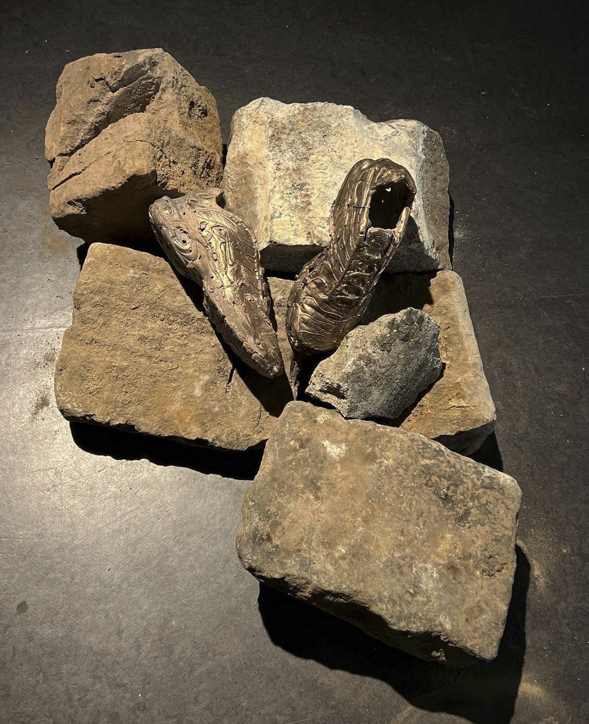 a pair of bronze nike sneakers lie amongst found blocks of pavement on floor