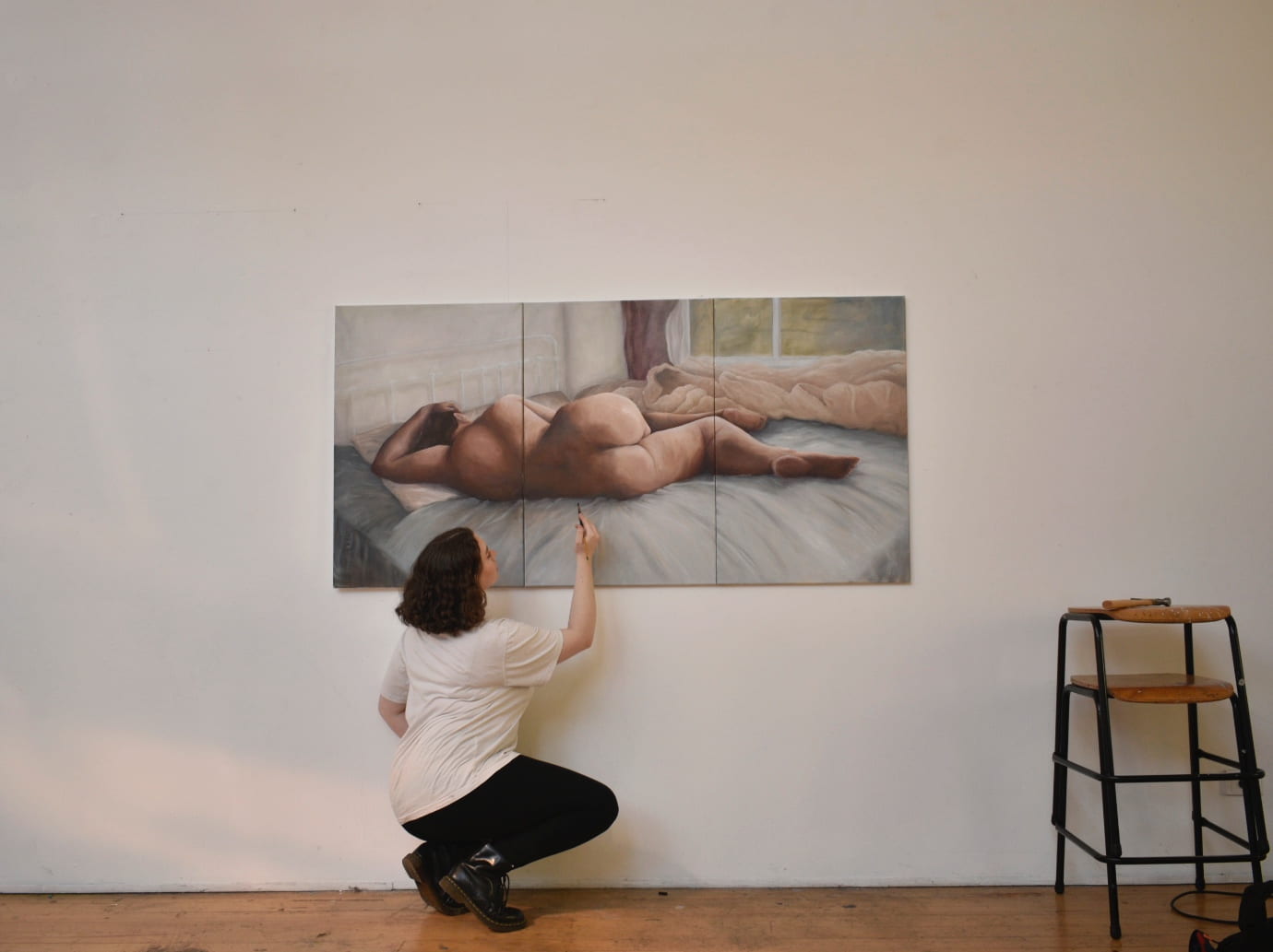 Artists, Tamara Perrett, squatting down and extending her arm up to work on the painting ‘Afterglow’