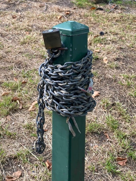 A green metal bollard with a tick silver chain wrapped around it. 