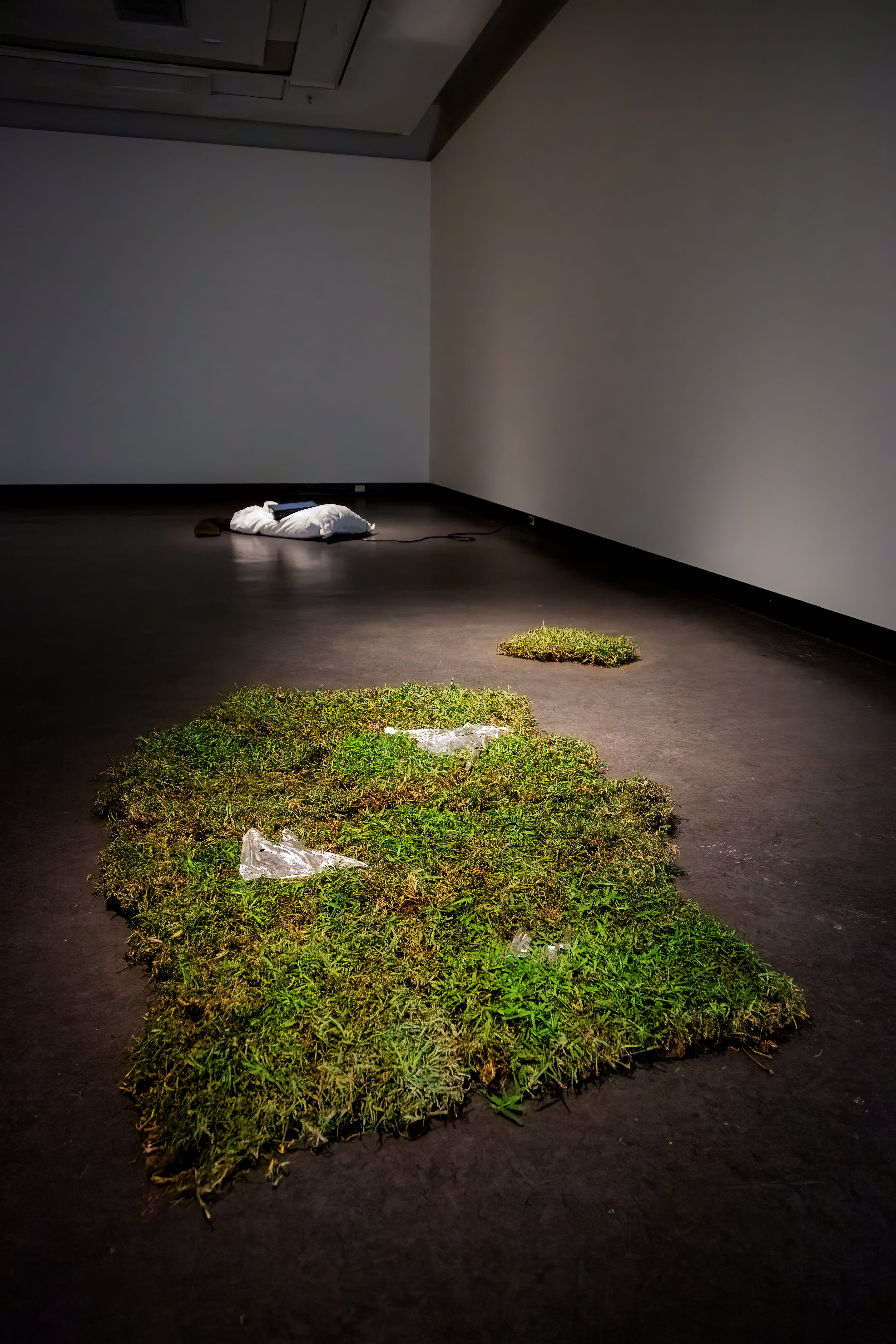 installation shot of two grass piles with pewter, a white sack with a tv can be seen in background