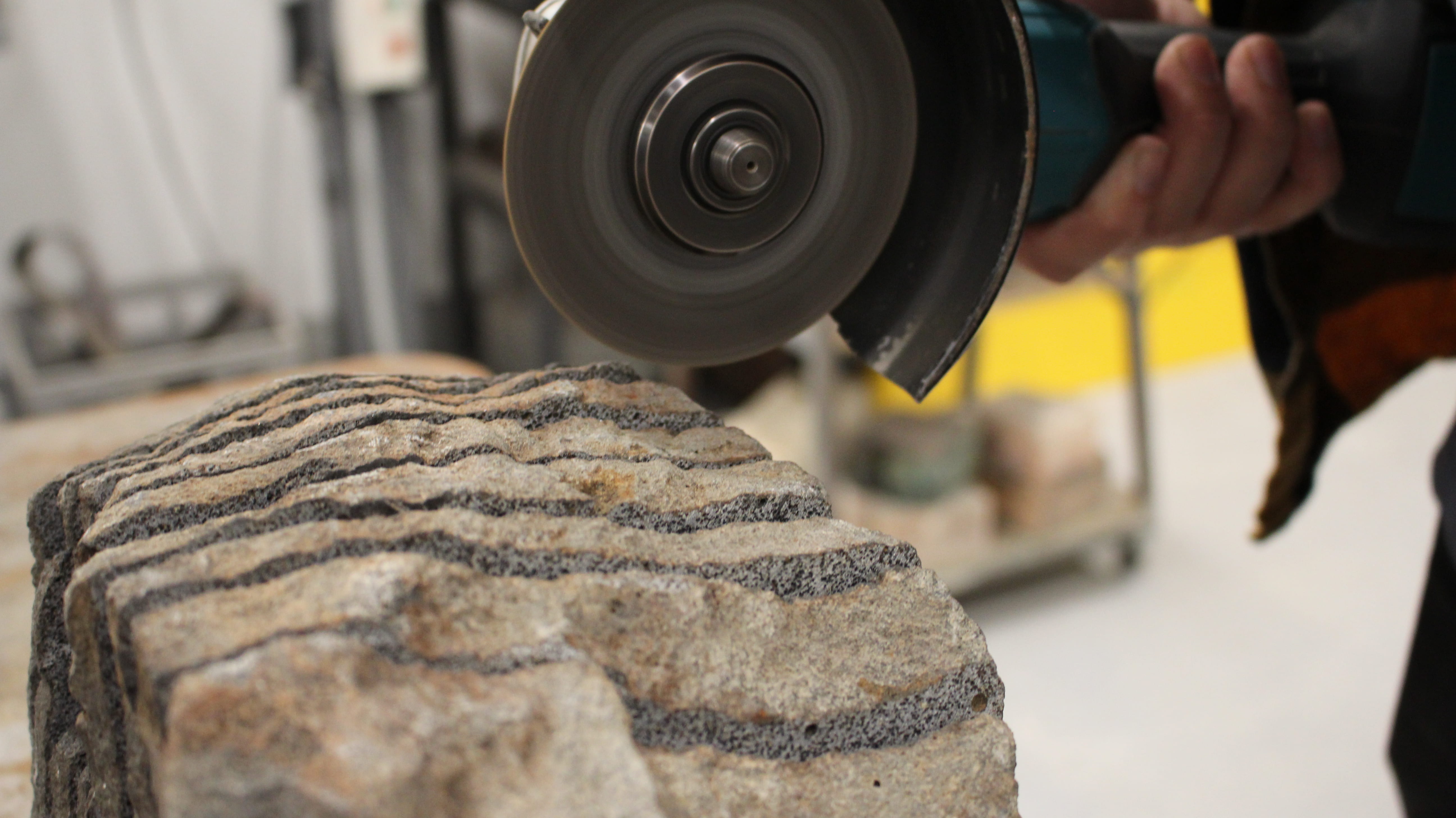 A photograph of an angle grinder positioned above a slotted stone block. In the background is workshop imagery.