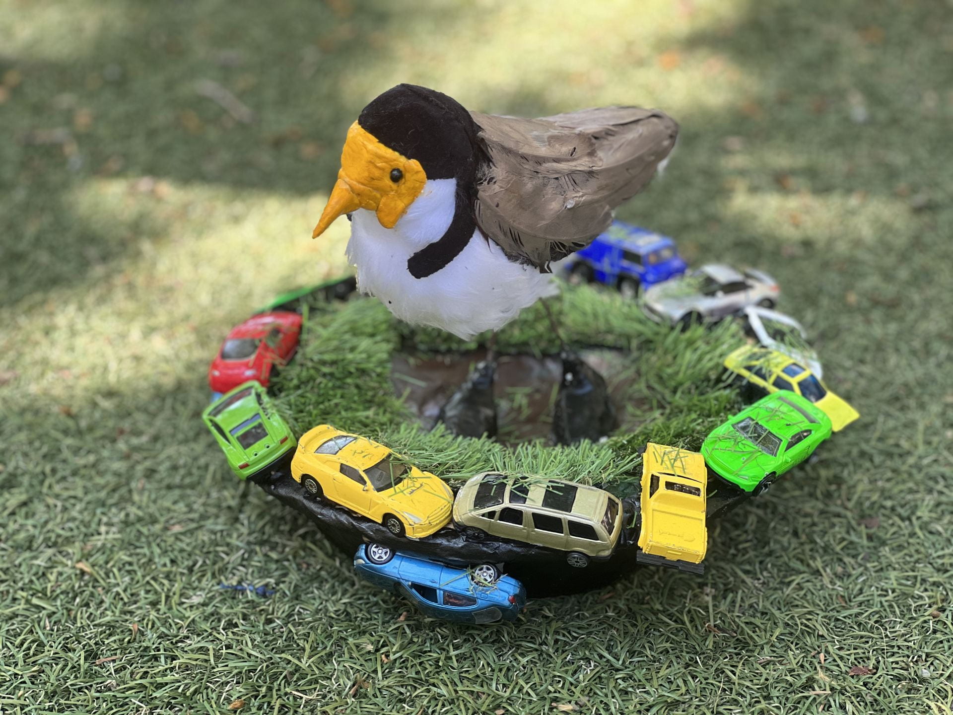 sculpture of a plover on a green base with cars around it