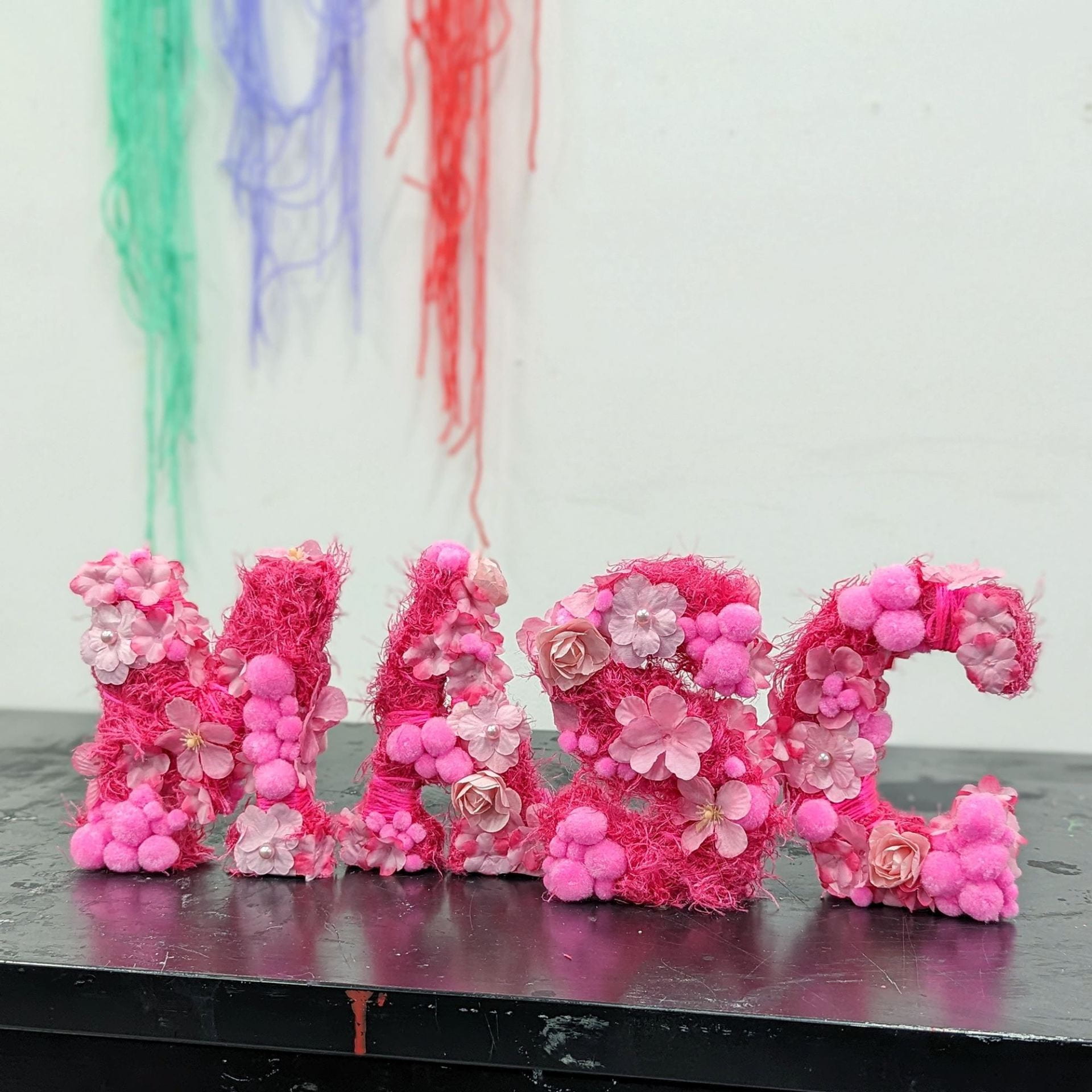 sculpture of the word MASC covered in pink flowers and pom-poms