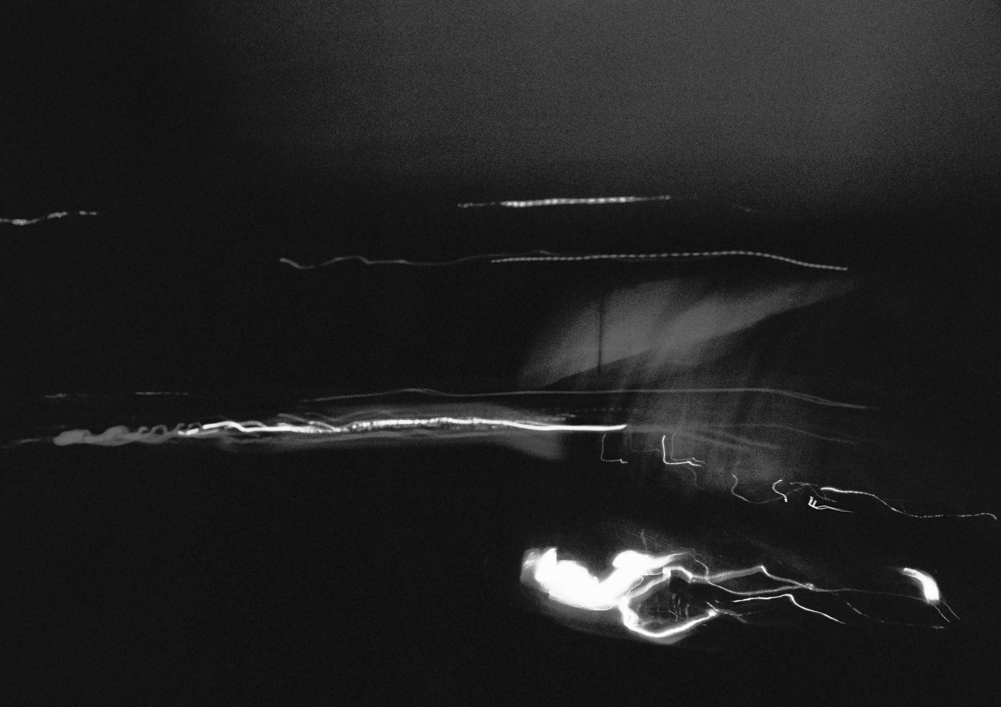 A black and white image. Blurred, slow-shutter, image of car lights passing by. 