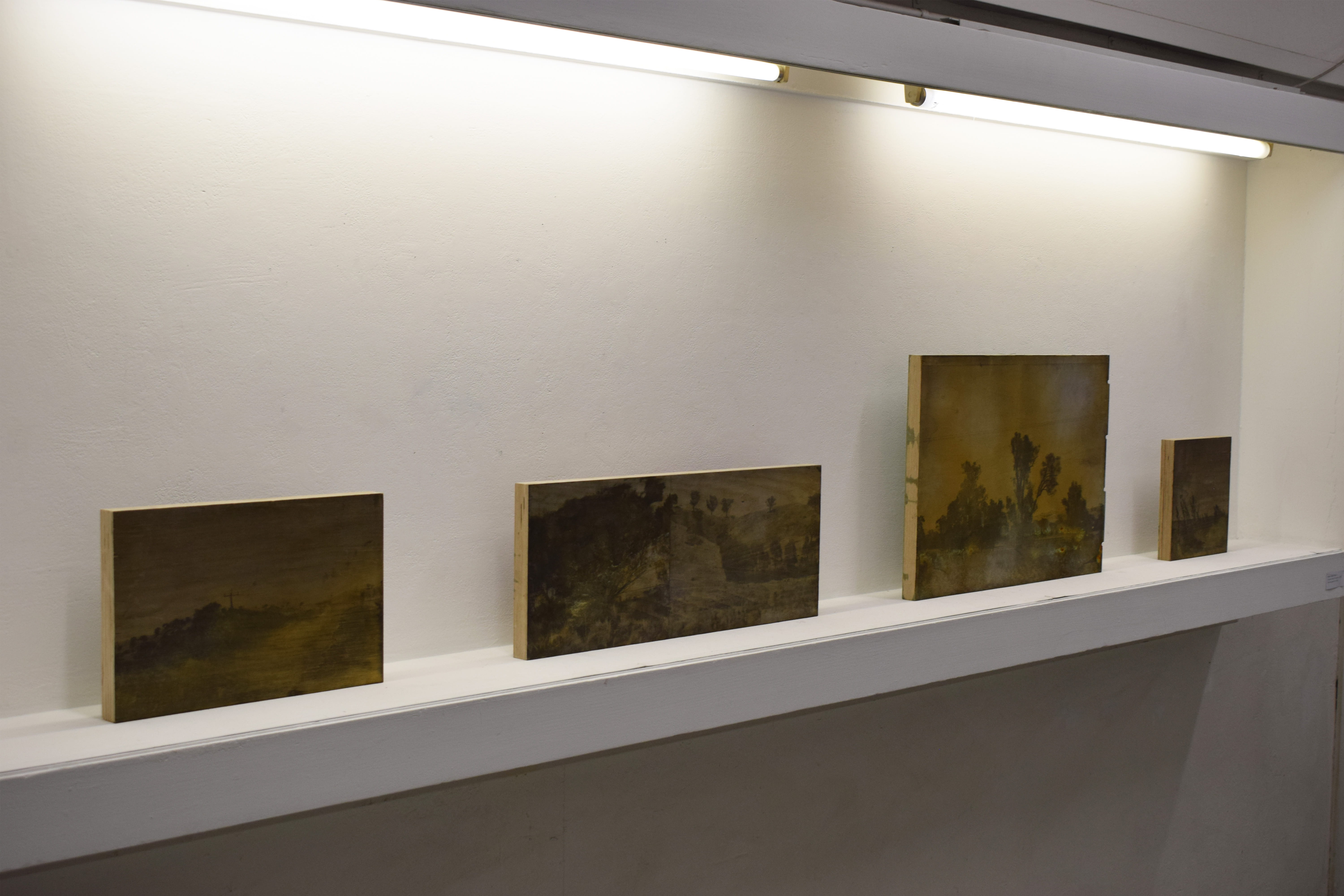 A line of greyscale on metal landscapes sit on a shape. Each is the size of a large postcard. 