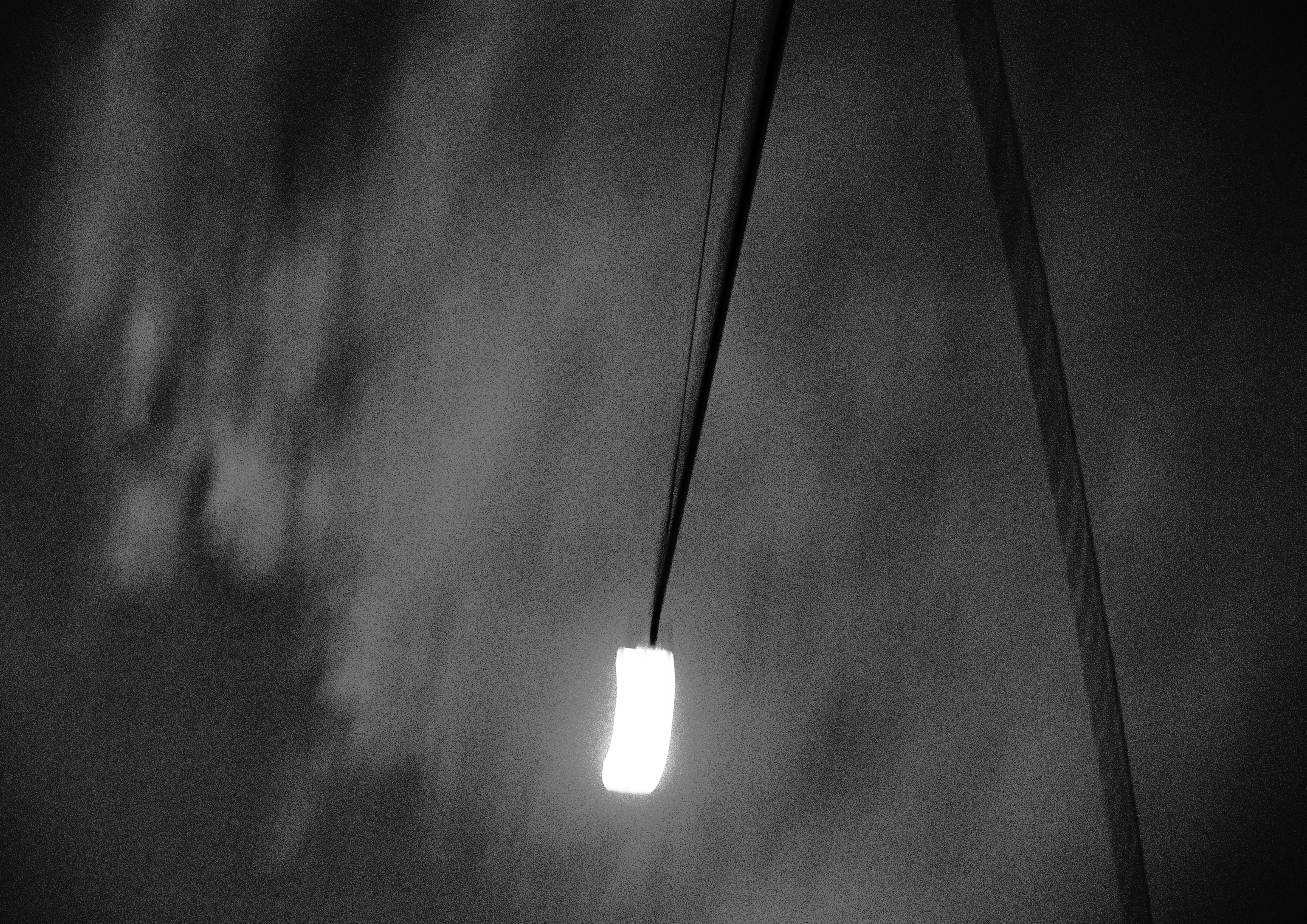 A blurry image of a street light. the image is black and white. The white of the light is blown out, no detail. dark skies and clouds in the background.