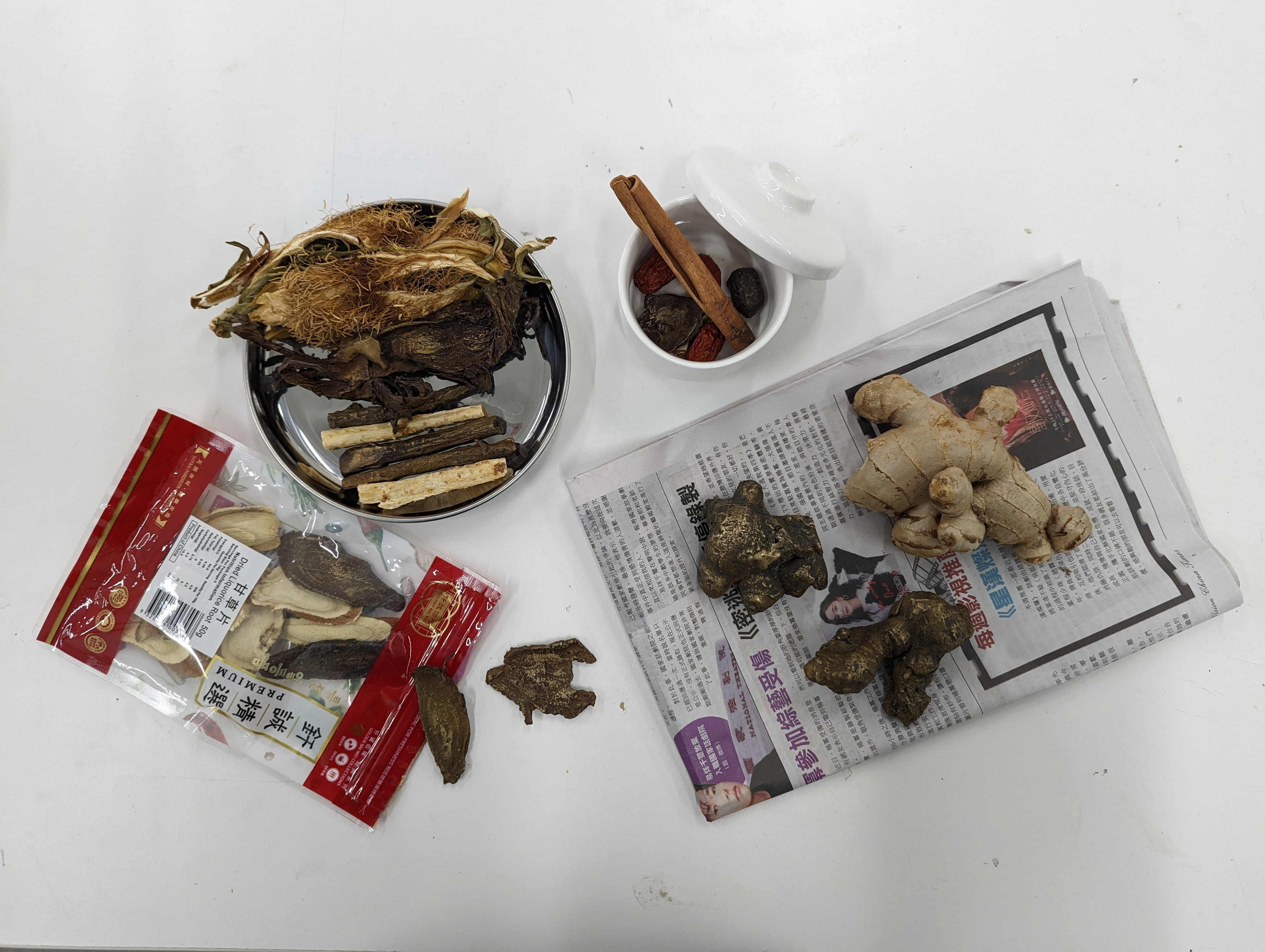 A mixed media assemblage of ingredient used in Chinese medicine with news paper sit on a table. Some of the ingredients are real and others are cast in bronze. 