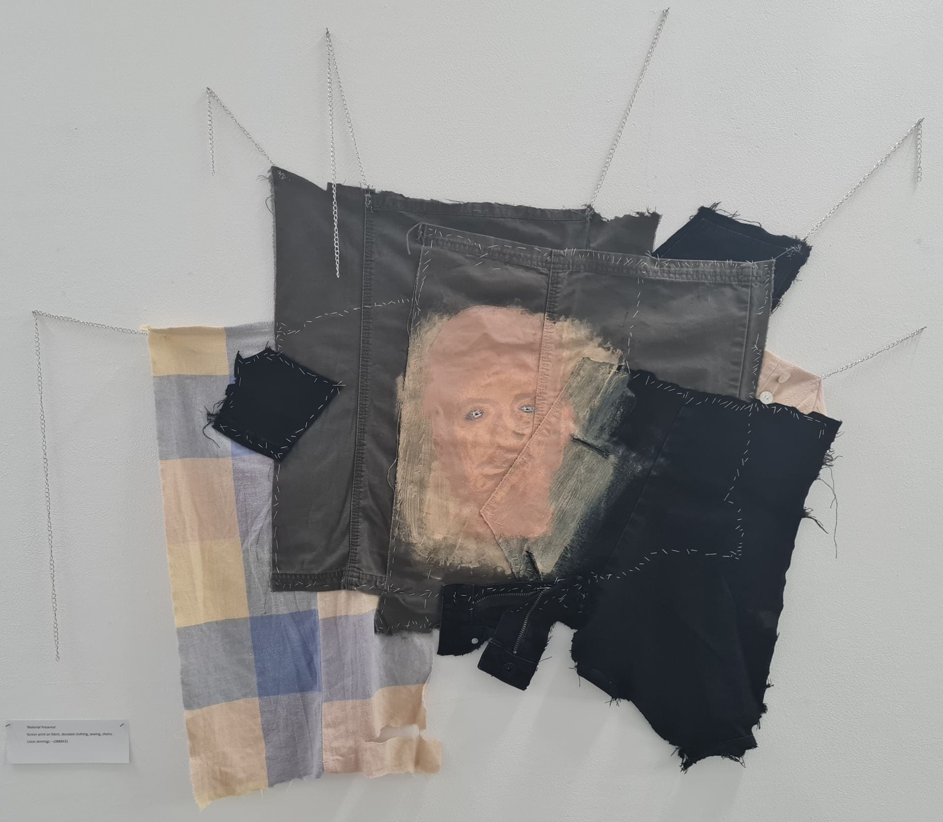 Sections of pants and shirts a stitched together unevenly to create a canvas. On the clothing a face has been painted.
