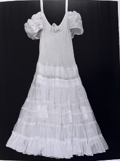 A white princess dress hangs in front of a black background. 