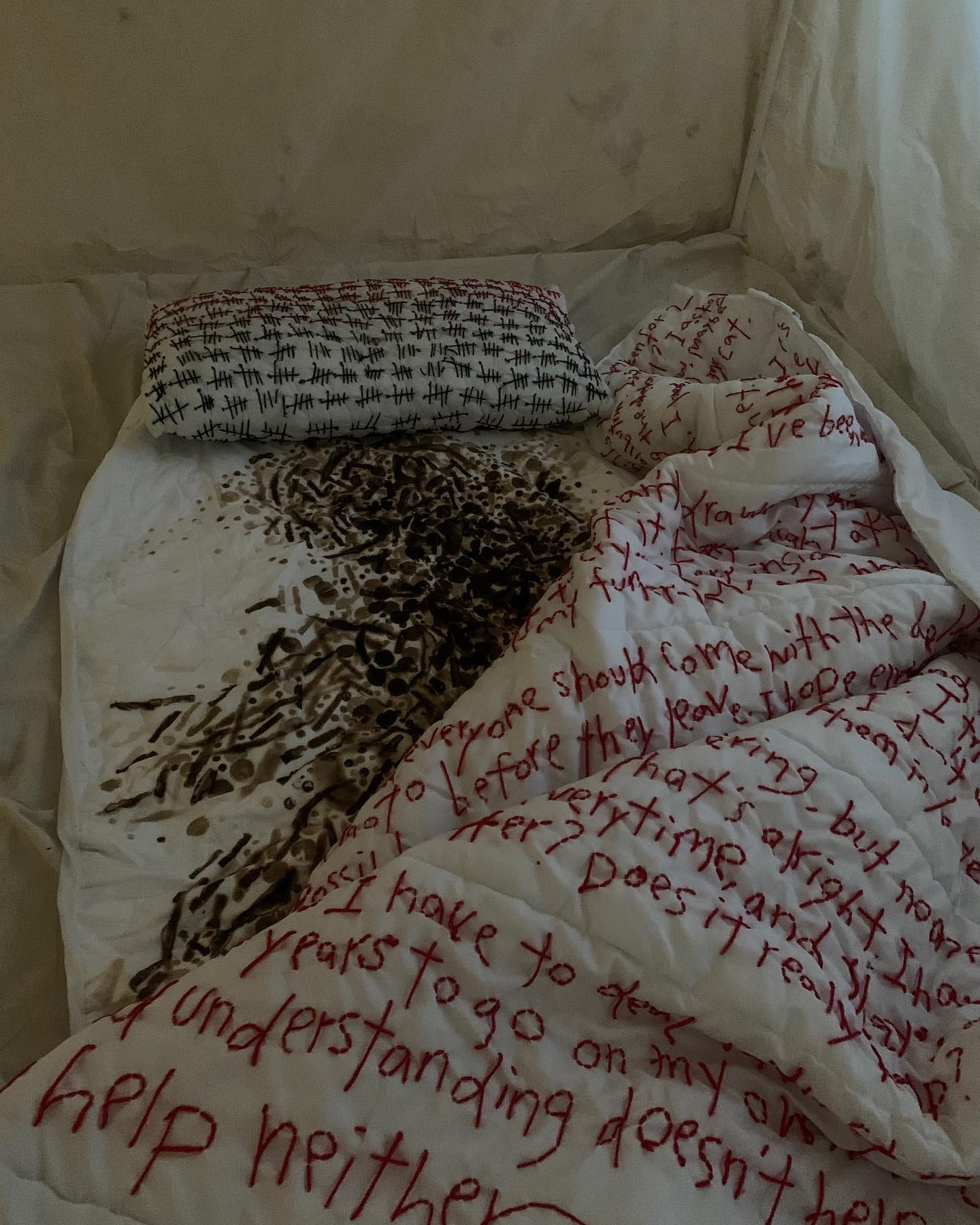 A bed sits on a floor with hand stitched text on the doona, pillow and sheets. 