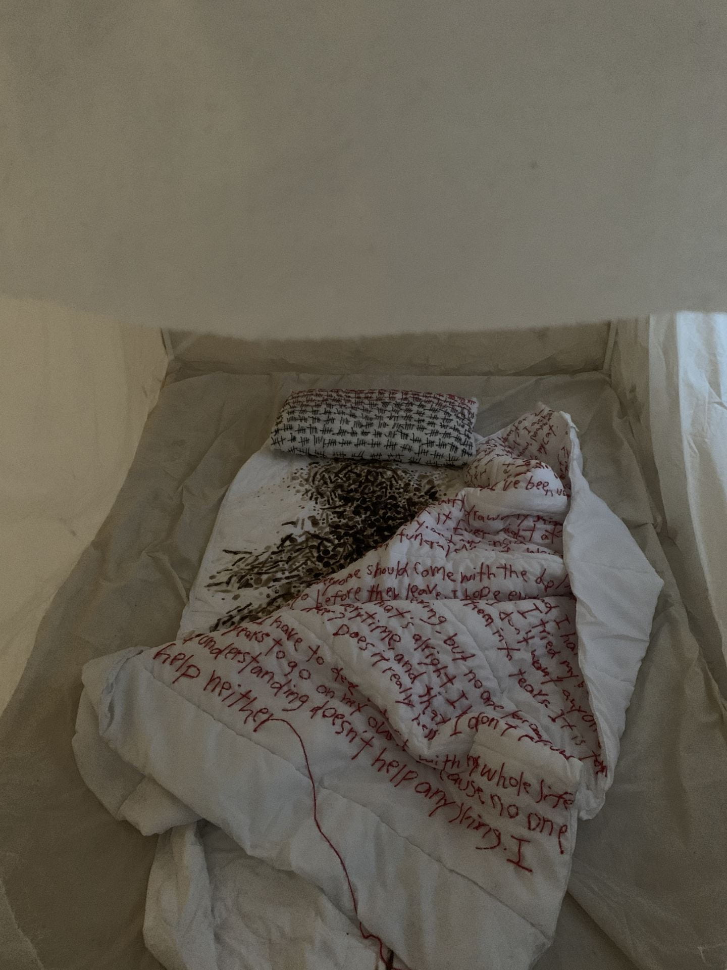 A bed sits on a floor with hand stitched text on the doona, pillow and sheets. 