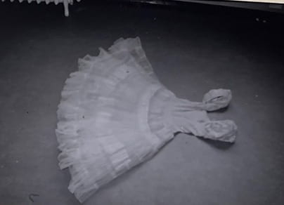 A white princess dress lays on the ground in a house. 